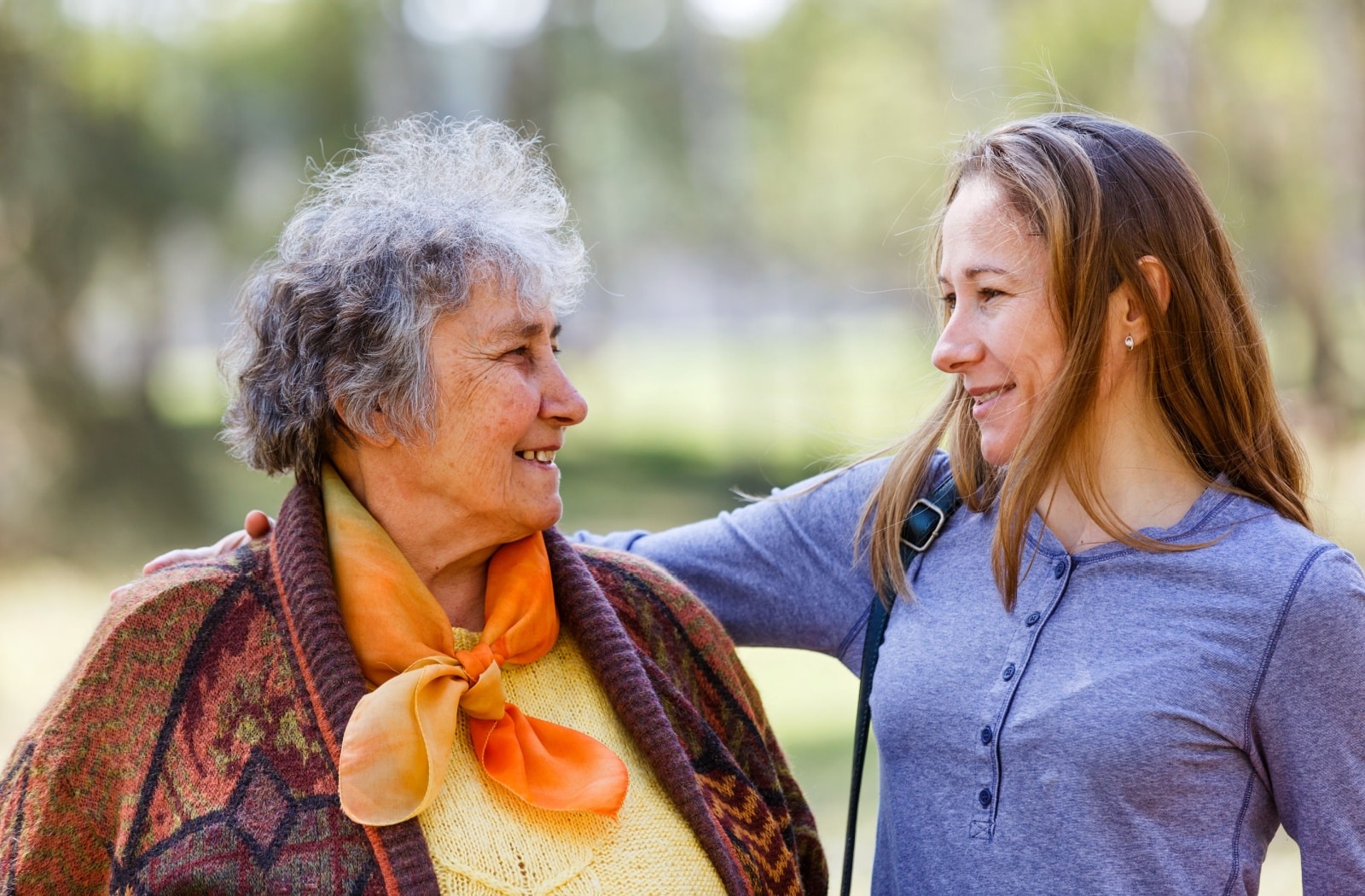 Younger woman visiting her elderly relative outdoors, sharing a moment of connection.