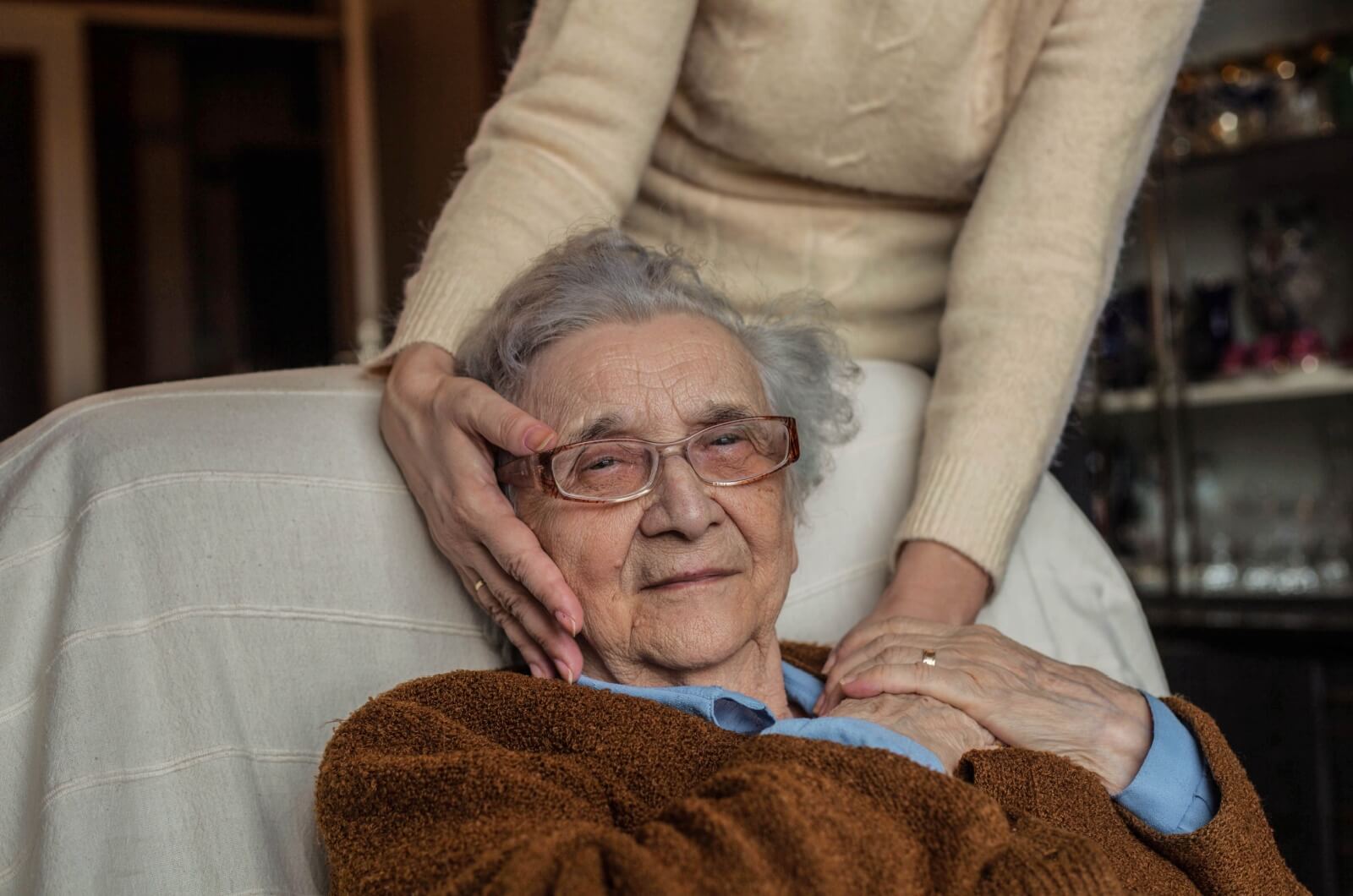 A loved one with Alzheimer's sitting in a sofa with a family caregiver touching their face and shoulder from behind.
