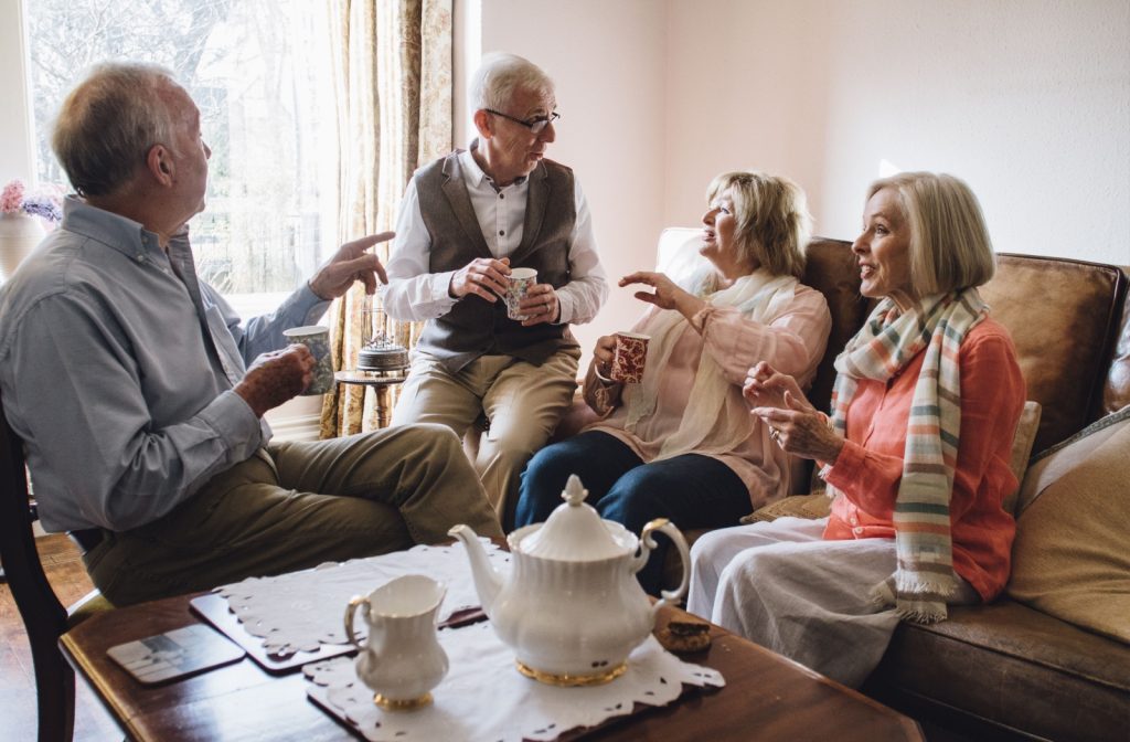 Seniors at a memory care community sitting in a common room enjoying a cup of tea and chatting with their friends