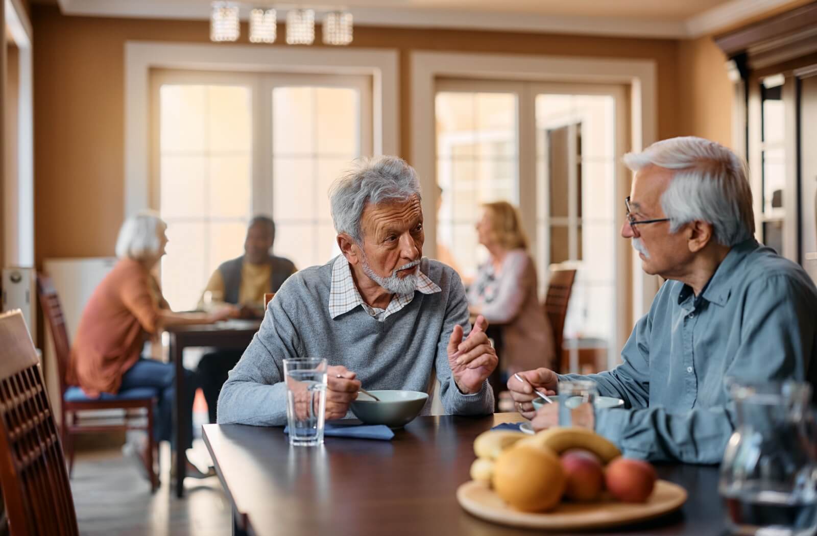 Seniors at a memory care community eating a bowl of soup for dinner and chatting with friends.
