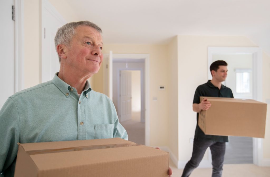 An adult helping their senior loved one move boxes into their new brightly lit home at a memory care community.